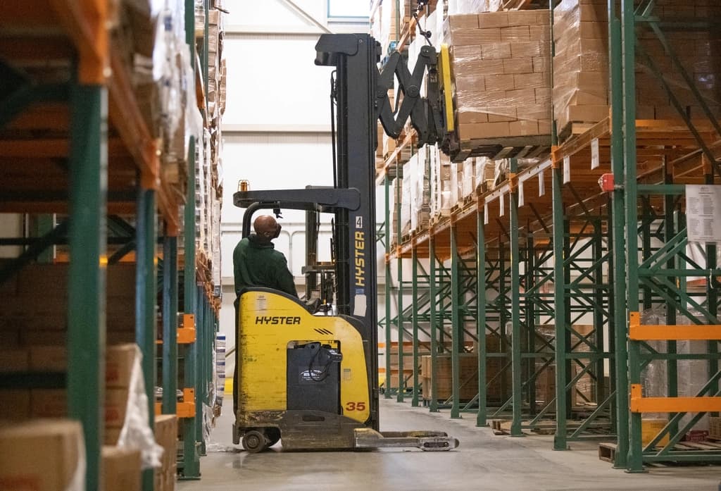 Reach truck lifting stock in a high-bay warehouse aisle