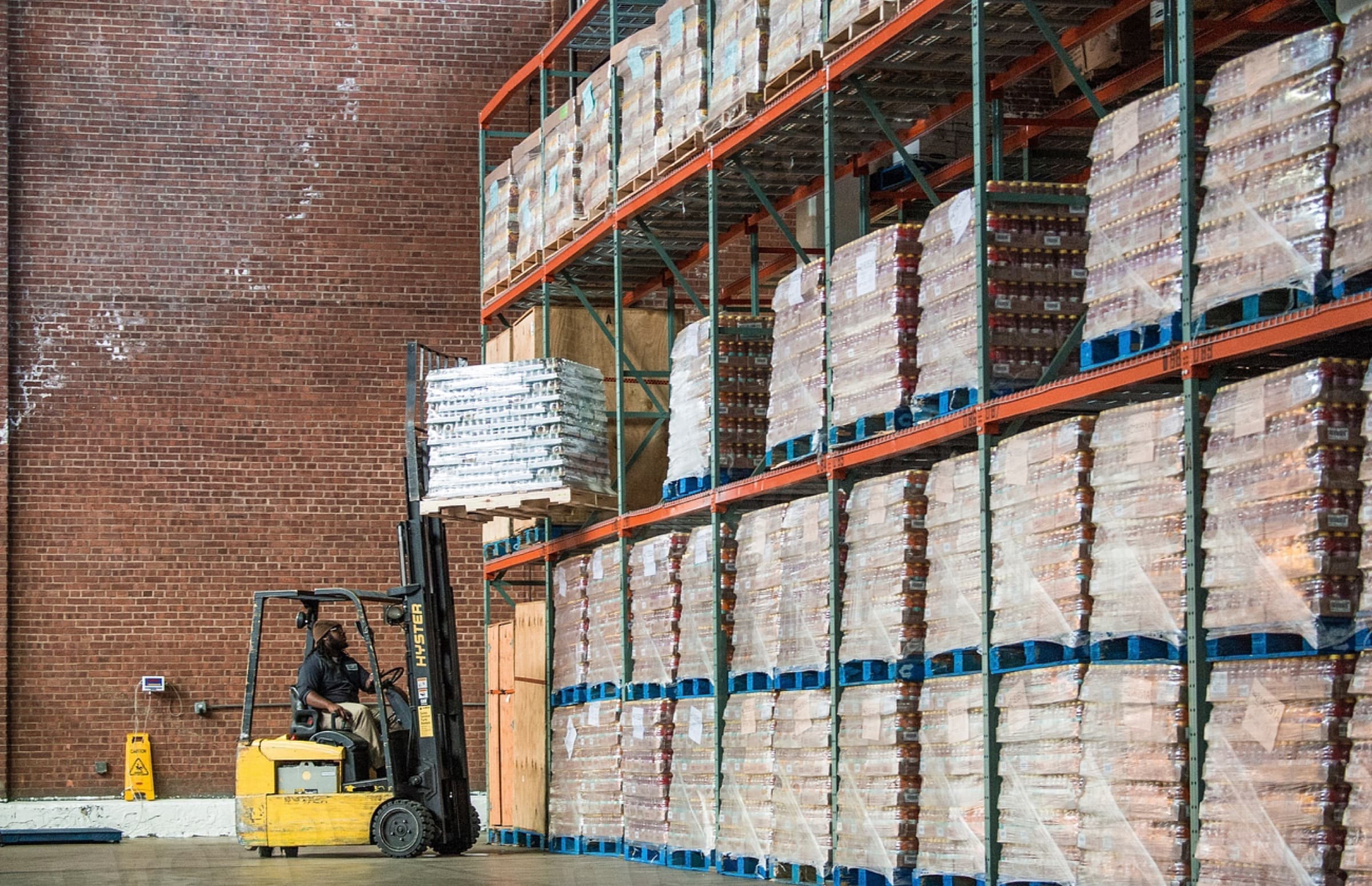 Forklift stacking pallets against warehouse racking